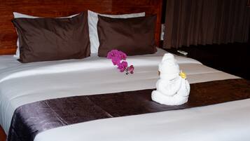 Un lit bien fait, avec une couette blanche, deux oreillers marron, une sculpture décorative en forme de serviette et des fleurs roses.