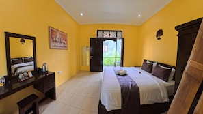 A hotel room with a bed, a desk, a mirror, and a door leading to a balcony. - Lemon Blossom Guest House (Ubud)