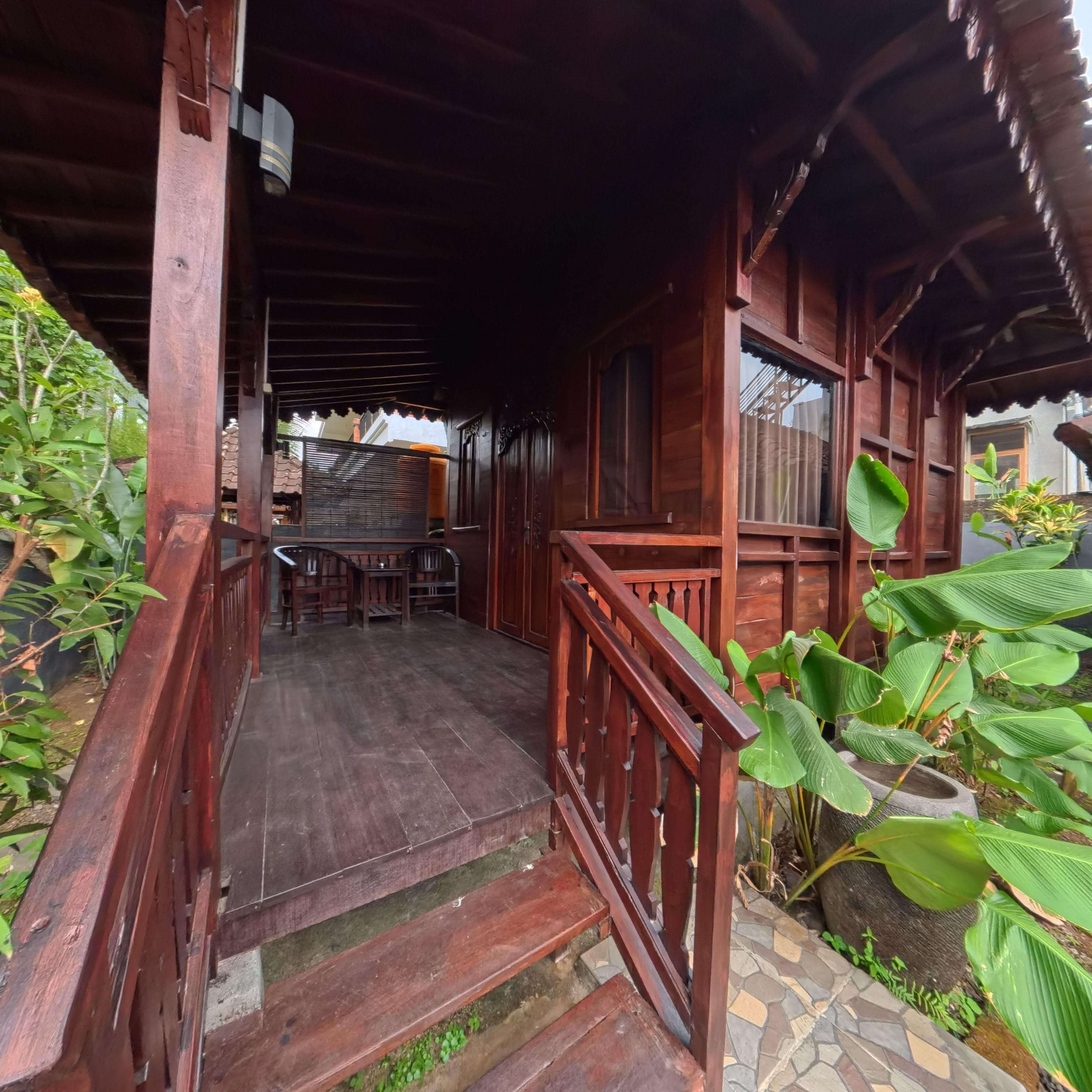 A wooden porch with a staircase leading to a covered area, surrounded by greenery.