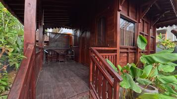 A wooden porch with a staircase leading to a covered area, surrounded by greenery.