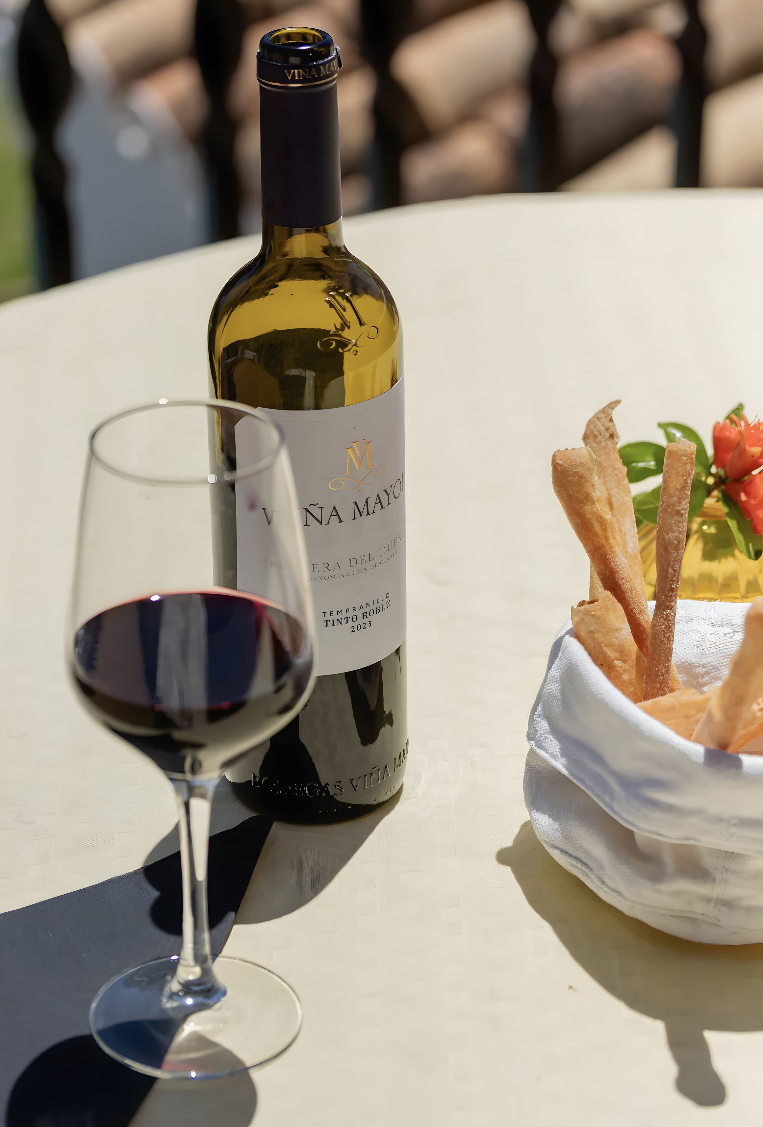 Une bouteille de vin, un verre de vin rouge et un panier de pain sur une table.