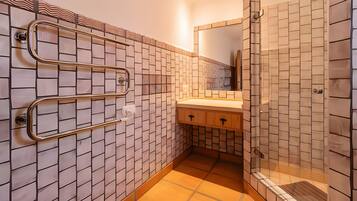 A bathroom with a tiled wall, a sink, and a shower area.