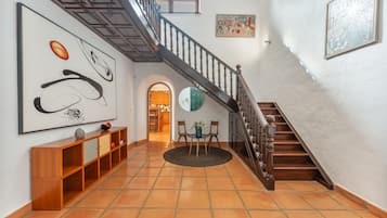 Een gang met een houten trap, een ronde tafel met stoelen en kunstwerken aan de muur.