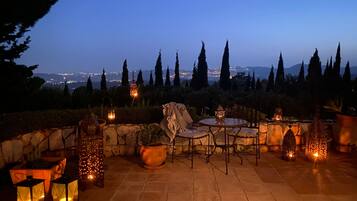 An outdoor patio area with stone flooring, round tables, and chairs, surrounded by decorative lanterns and potted plants.