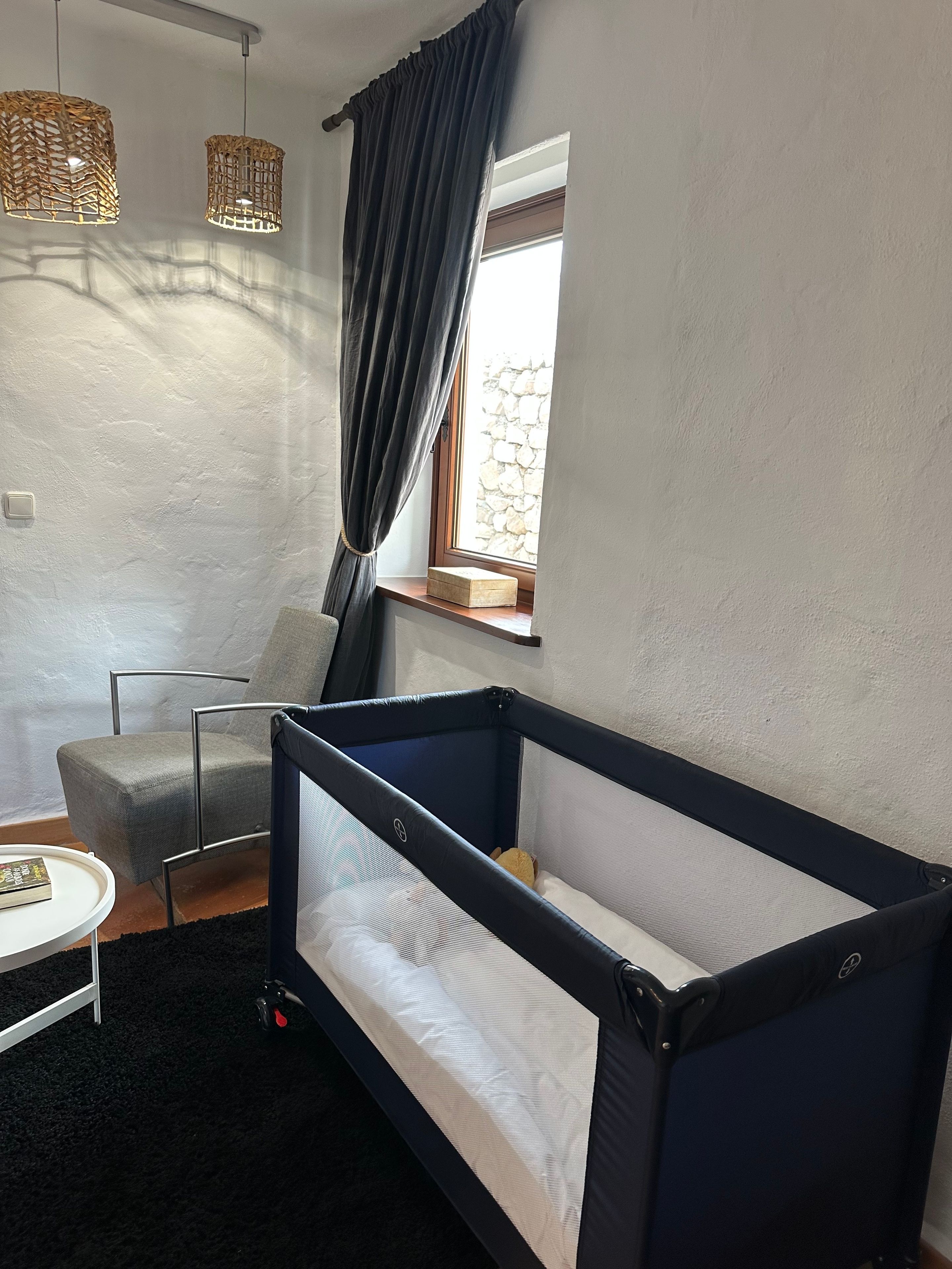 Una habitación con una cama individual, una silla, una mesita y un ventanal con cortinas.