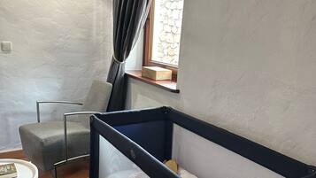 Una habitación con una cama individual, una silla, una mesita y un ventanal con cortinas.