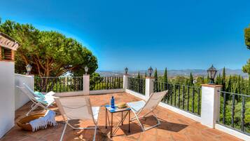 A terrace with two white lounge chairs, a small table, and a view of the landscape.