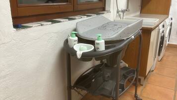 A compact kitchen with a window, a washing machine, and a small table with toiletries.