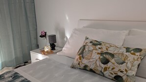 Ein ordentlich bezogenes Bett mit einem Blumenkissen, ein Nachttisch mit einer Lampe, einem Buch und einer Blumenvase.