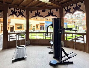 Ginásio com equipamentos de exercício e amplas janelas com vista para um pátio.