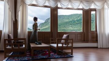 A room with large windows, wooden furniture, and a view of a mountainous landscape.