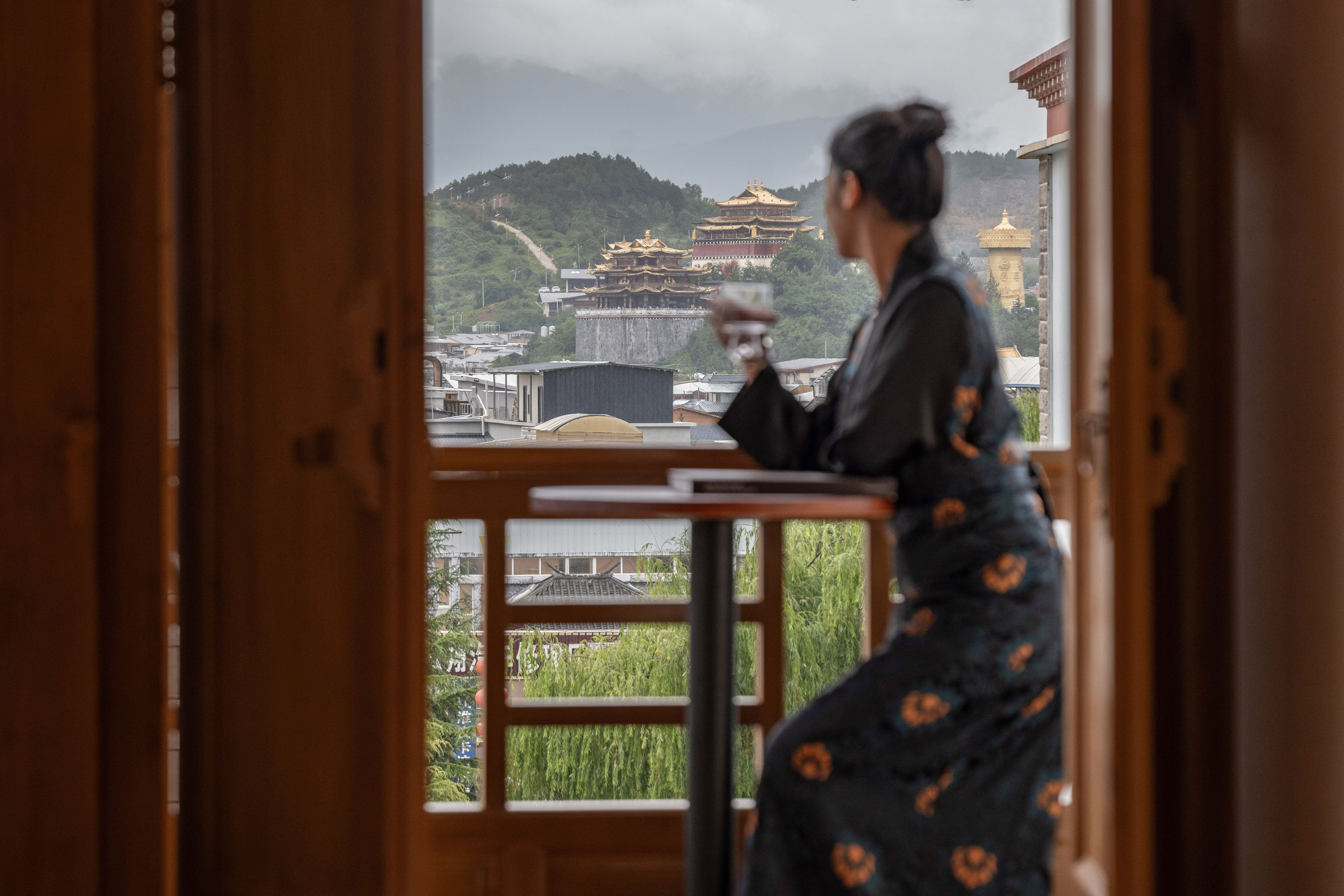 Una persona vestida con traje tradicional de pie junto a una ventana con vistas a un templo y una pagoda.