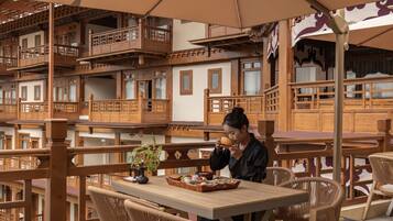A traditional wooden balcony with multiple levels, furnished with wicker chairs and a table, overlooking a courtyard.