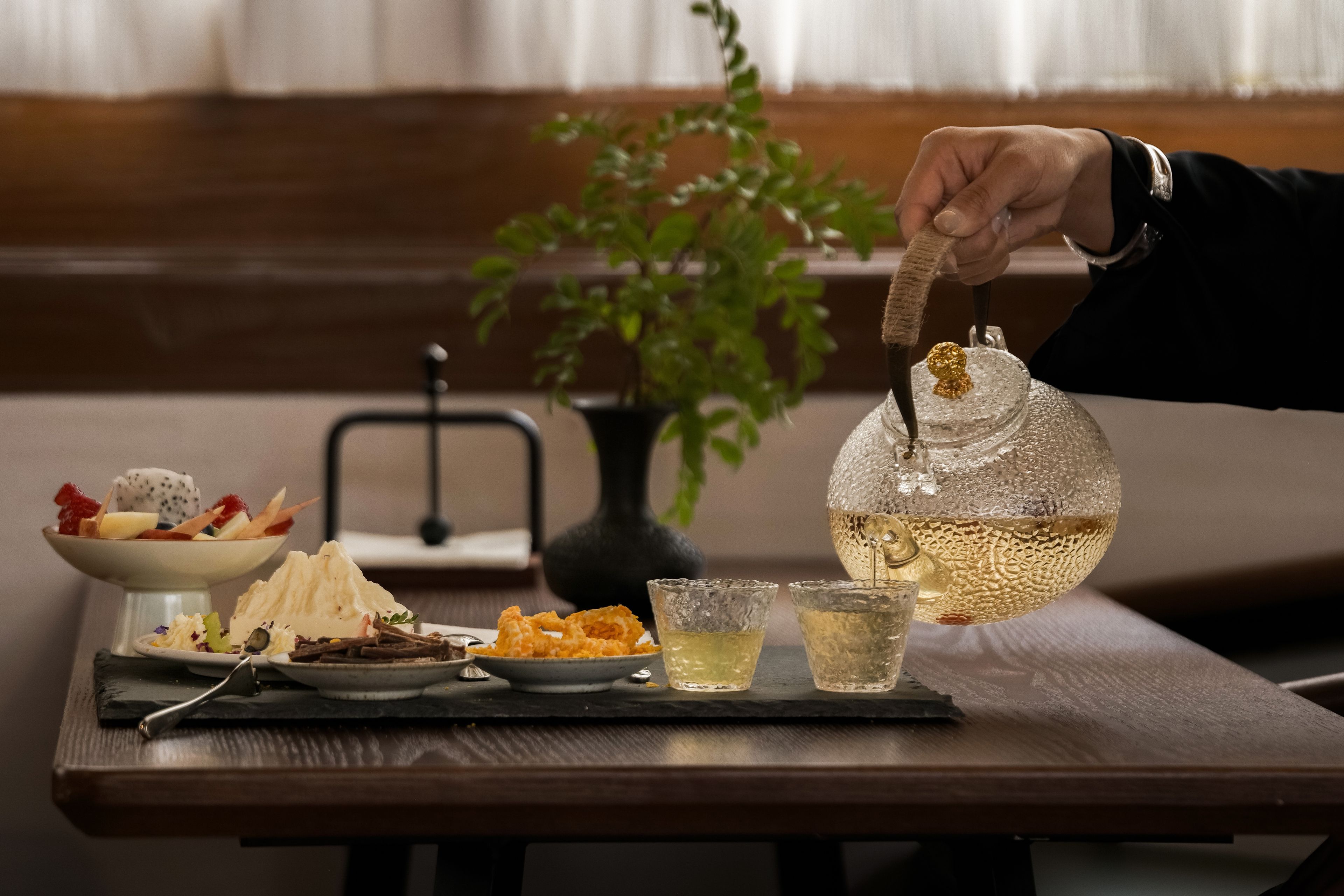 Una mesa con una tetera, vasos y una bandeja de comida.
