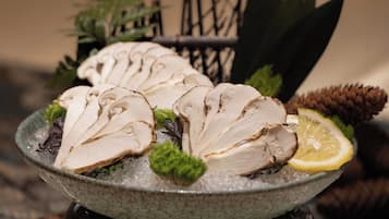Un tazón de pechuga de pollo en rodajas sobre hielo con limón y vegetales verdes.