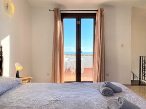 A hotel room with a bed, a lamp, a view of the beach, and a balcony with chairs. - Apartment in Nerja With Sea & Mountain Views (Nerja)