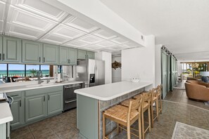 Een moderne keuken met een groot eiland, barkrukken en uitzicht op de oceaan.