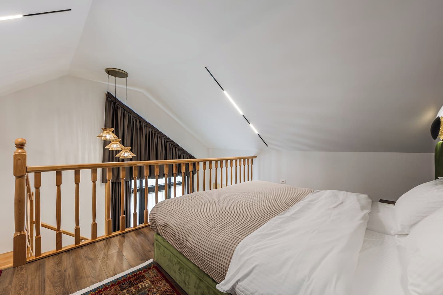 Ein Schlafzimmer mit schrägem Dach, einer Holztreppe, einem Bett mit weißer Bettwäsche und einer Hängeleuchte.