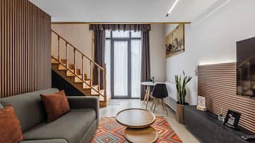 Ein modernes Wohnzimmer mit einer Couch, einem Couchtisch, einem Essbereich mit Stühlen, einer Treppe und einem Fernseher an der Wand.