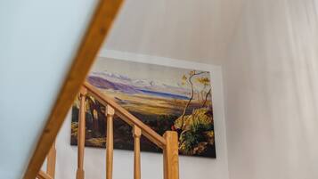 Een trap met houten spijlen die leidt naar een kamer met een groot landschap op de muur.