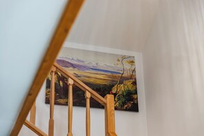 Eine Treppe mit Holzspindeln führt zu einem Raum, in dem sich ein großes Landschaftsbild an der Wand befindet.