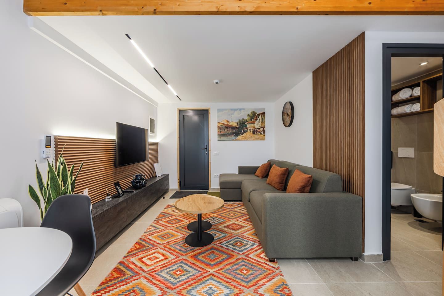 Een moderne woonkamer met een grijze bank, een televisie bevestigd aan een houten paneel, een kamerkleed met een patroon en een houten plafond.