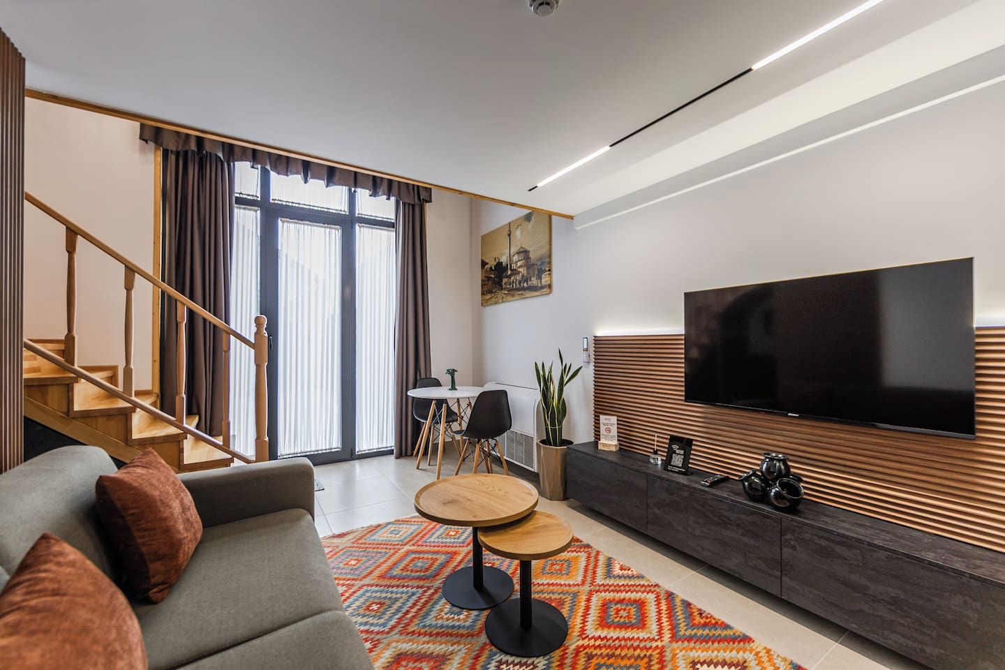 A modern living room with a sofa, coffee table, and a flat-screen TV mounted on a wooden panel wall.