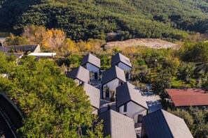 A modern building with multiple levels and a sloped roof, surrounded by dense forest and a small body of water. - Muraga Villas 6 | Sofra (Tiranë)