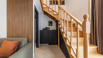 A modern living room with a wooden staircase, a grey sofa, and a dark cabinet.