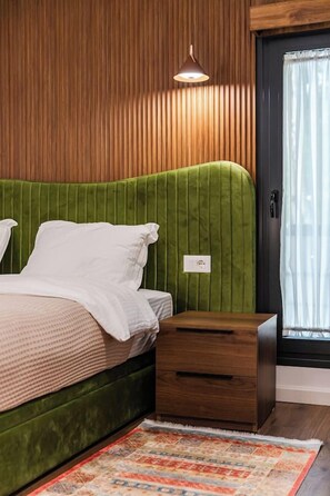 Ein Schlafzimmer mit einem grünen, gepolsterten Kopfteil, einem Nachttisch aus Holz und einem gemusterten Teppich.