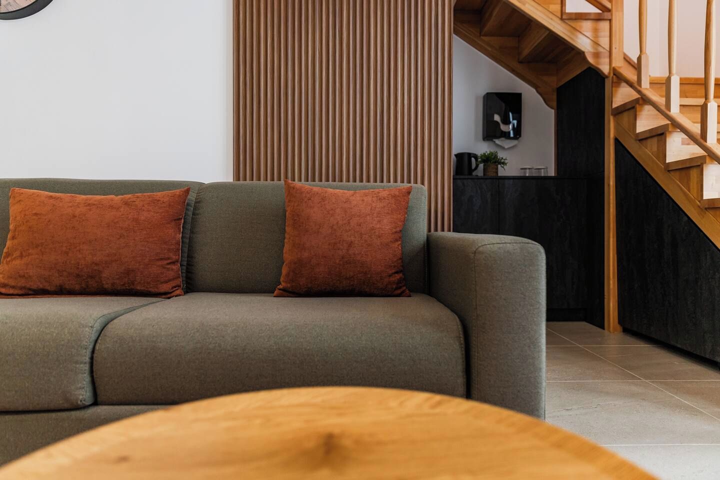 A modern living room with a sofa, two cushions, a wooden coffee table, and a staircase.