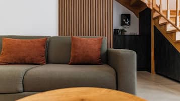 A modern living room with a sofa, two cushions, a wooden coffee table, and a staircase.