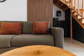 Una sala moderna con un sofá, dos cojines, una mesa de centro de madera y una escalera.