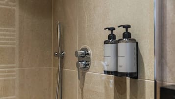 A shower with a chrome faucet and a handheld showerhead. There are two bottles of body lotion on the wall.