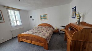 Ein Schlafzimmer mit einem hölzernen Bett, einem Nachttisch, einem Sessel, einer Kommode und einem Fenster mit Vorhängen.