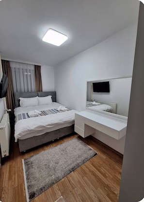 A modern hotel room with a bed, bedside table, TV, and a small desk with drawers. - Central Bus Station Apartment (Prishtinë)