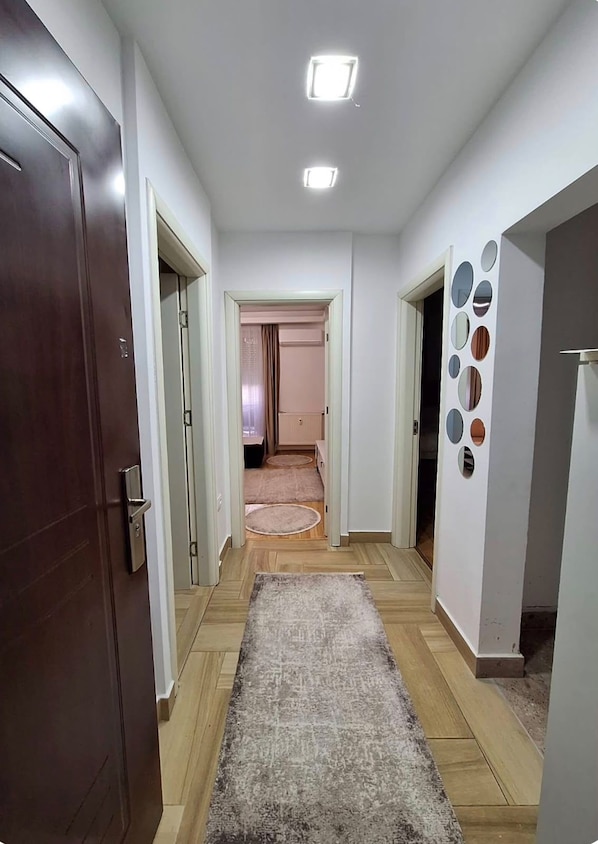A hallway with a wooden floor, a rug, and a door on the left. - Central Bus Station Apartment (Prishtinë)