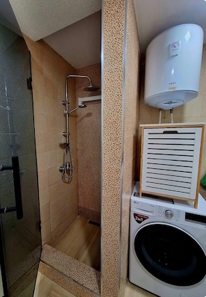 A bathroom with a shower, a washing machine, and a water heater. - Central Bus Station Apartment (Prishtinë)