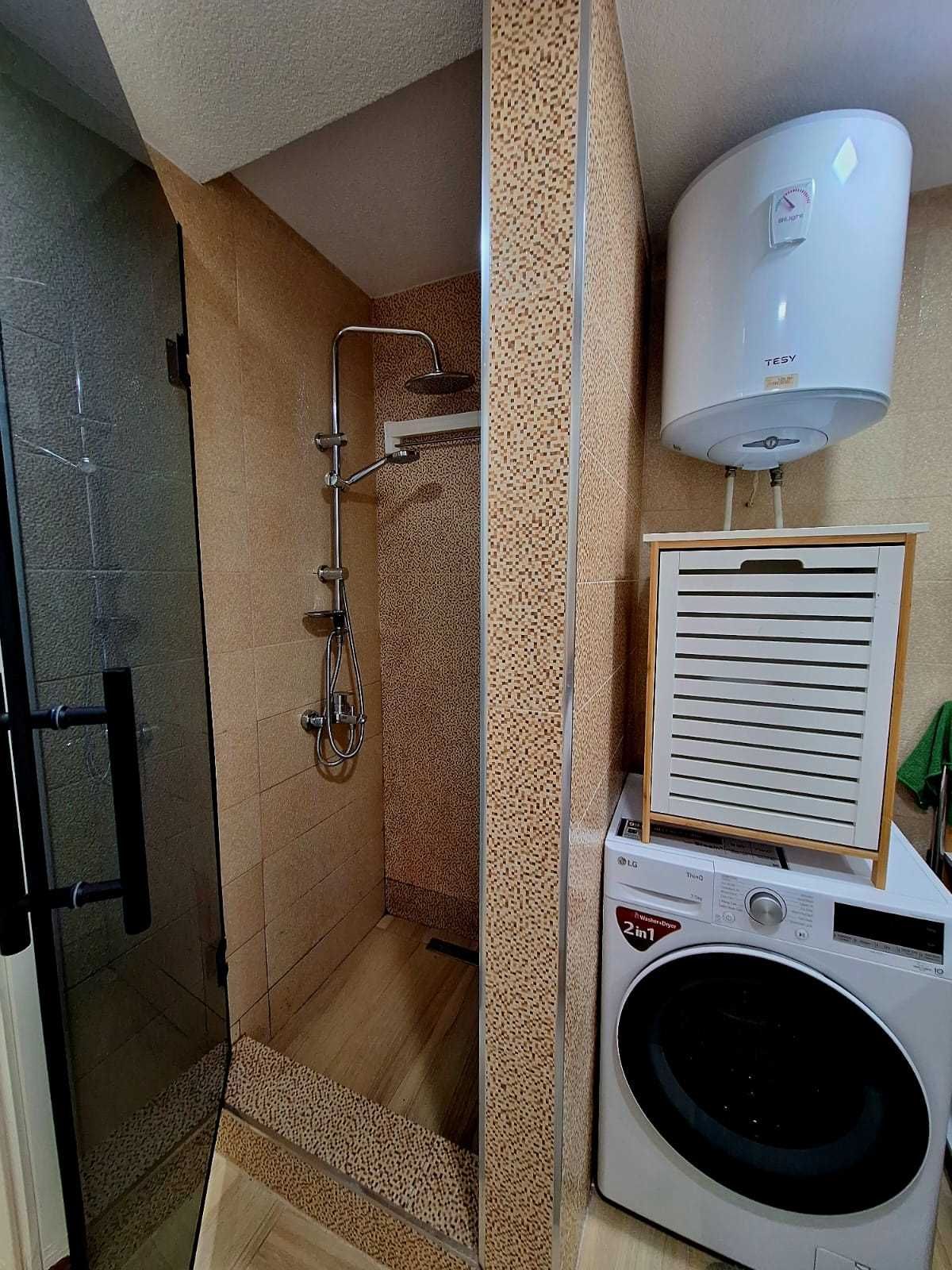 Casa de banho com cabine de chuveiro em vidro, esquentador branco e máquina de lavar e secar empilhadas.