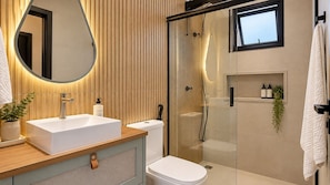 A modern bathroom with a large mirror, a sink, a toilet, and a glass-enclosed shower. - STUDIO 05 (Vinhedo)