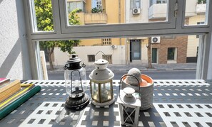 A balcony with a view of buildings and a street, featuring a table with decorative lanterns and a patterned metal railing. - Athens Culture Spot near Museum & Park by ΜΡS (Athina)