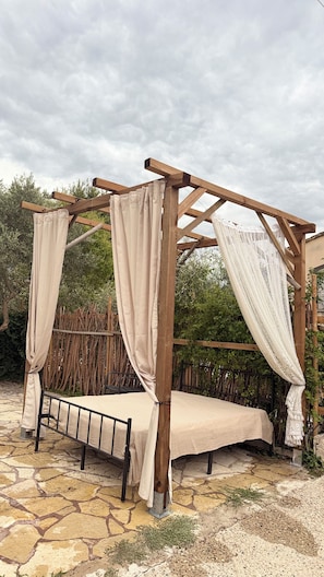 A wooden pergola with a bed underneath, surrounded by stone flooring and greenery. - A house in a quiet location in Provence with a pool, BBQ, and bike paths—pets welcome 🐾🚲🌿 (Loriol-du-Comtat)