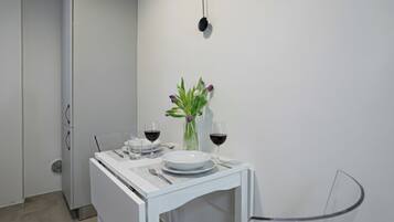 Ein kleiner, moderner Essbereich mit einem weißen Tisch, gedeckt für zwei Personen, mit einer Blumenvase und zwei Gläsern Rotwein.