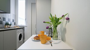Een keuken met een wasmachine, een koffiezetapparaat, een bord met croissants en een vaas met bloemen.