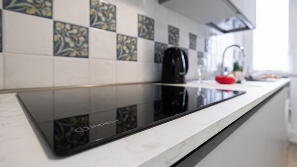 Een moderne keuken met een zwart inductiekookveld, witte tegels met bloemenmotieven en een roestvrijstalen waterkoker.
