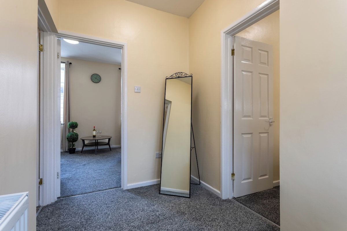 A hallway with carpeted flooring, a door, and a mirror leaning against the wall.