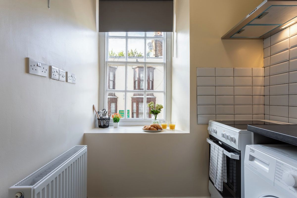A kitchen with a window, a radiator, a washing machine, and a tiled backsplash.