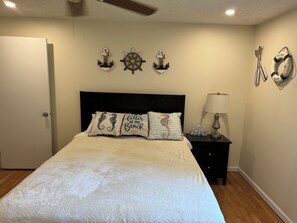 A bedroom with a bed, a nightstand, a lamp, and wall decorations including anchors and a welcome sign. - Perfect 3-bedroom house with AC in charming Falmouth (Falmouth)