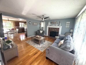 A spacious living room with a fireplace, a dining area, and a kitchen in the background. - Perfect 3-bedroom house with AC in charming Falmouth (Falmouth)