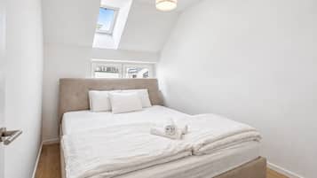 Een slaapkamer met een bed, kussens, een opgerolde handdoek, een raam en een dakraam.